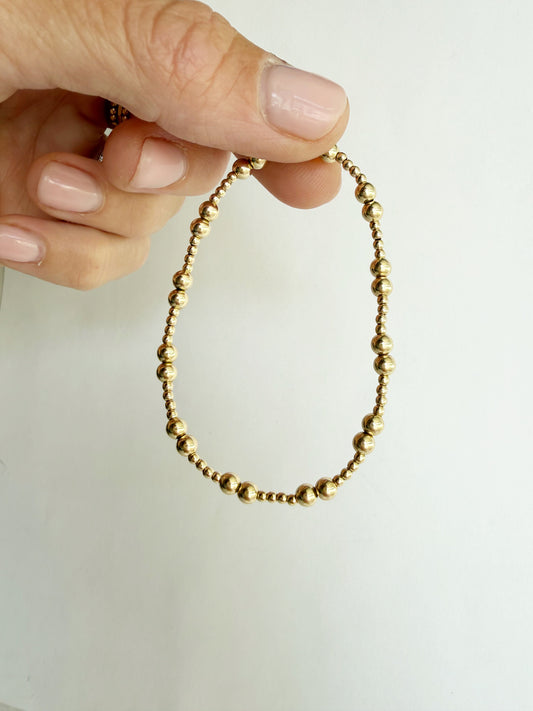The Demi bracelet held between fingers, showing the mixed gold bead pattern